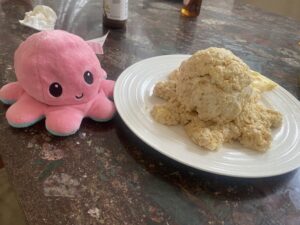 A pink octopus plush next to a plate with a rice krispie octopus on it